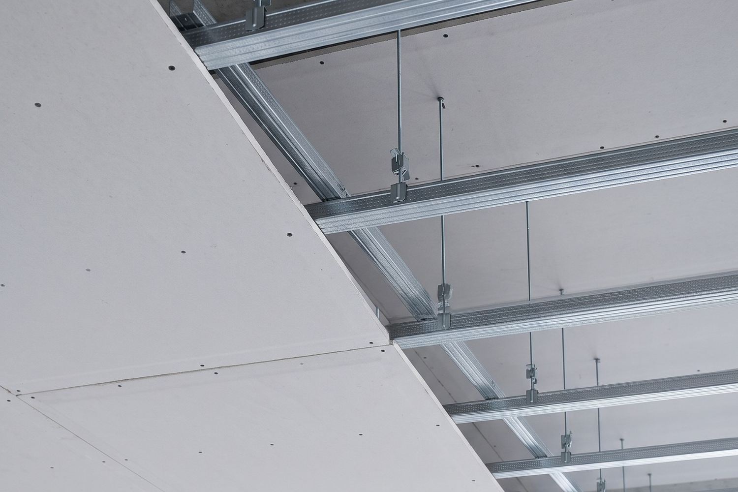 Forro de drywall em montagem, com os perfis F530 suspensos por pendurais e parte da placa já fechada