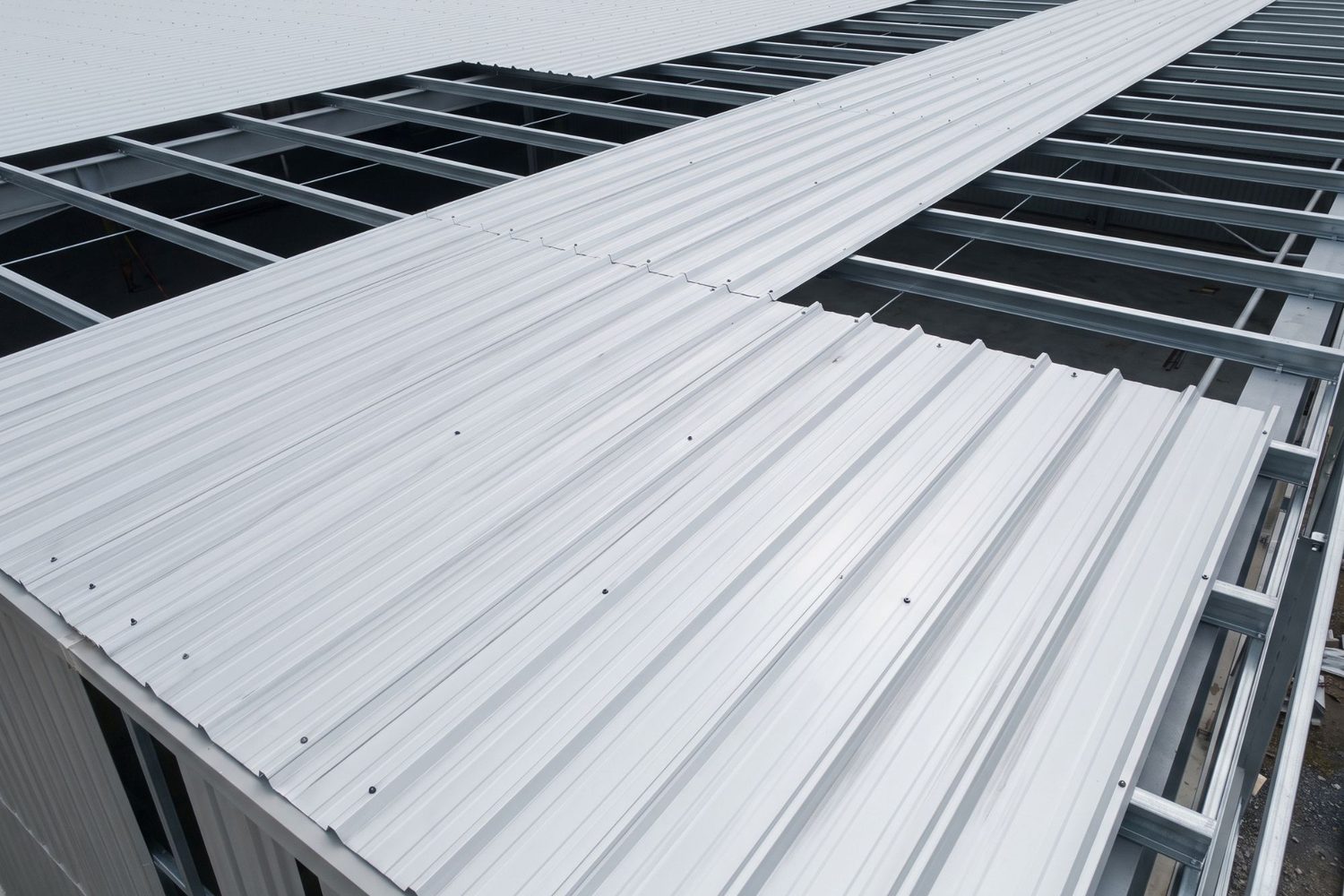 Cobertura metálica em montagem: telhas trapezoidais sendo assentadas sobre as terças e parafusadas na crista da onda